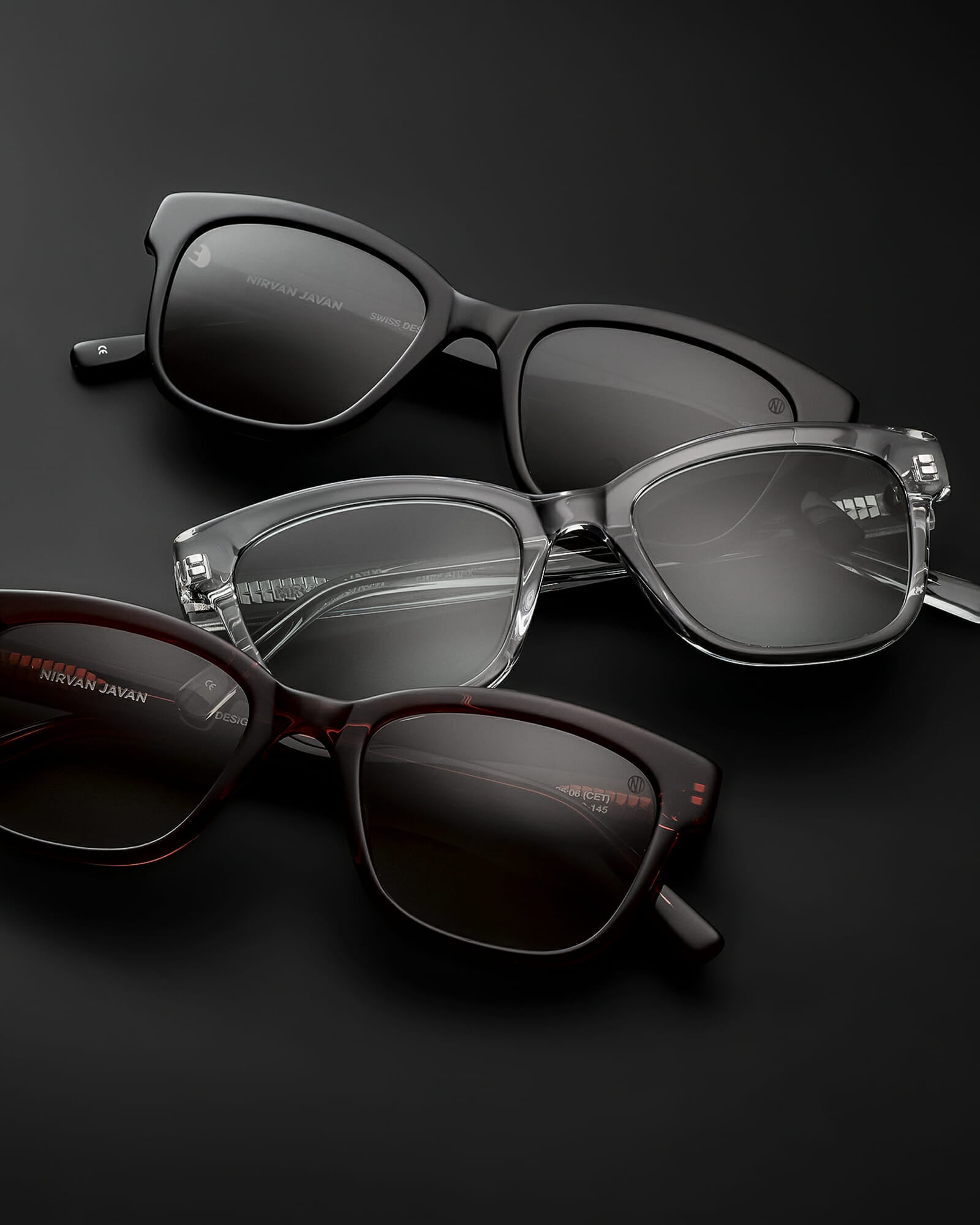 Three cat eye acetat shades, one in black with grey lenses, one in brown with brown lenses and one in transparent with grey lenses on a black background, the frames are folded