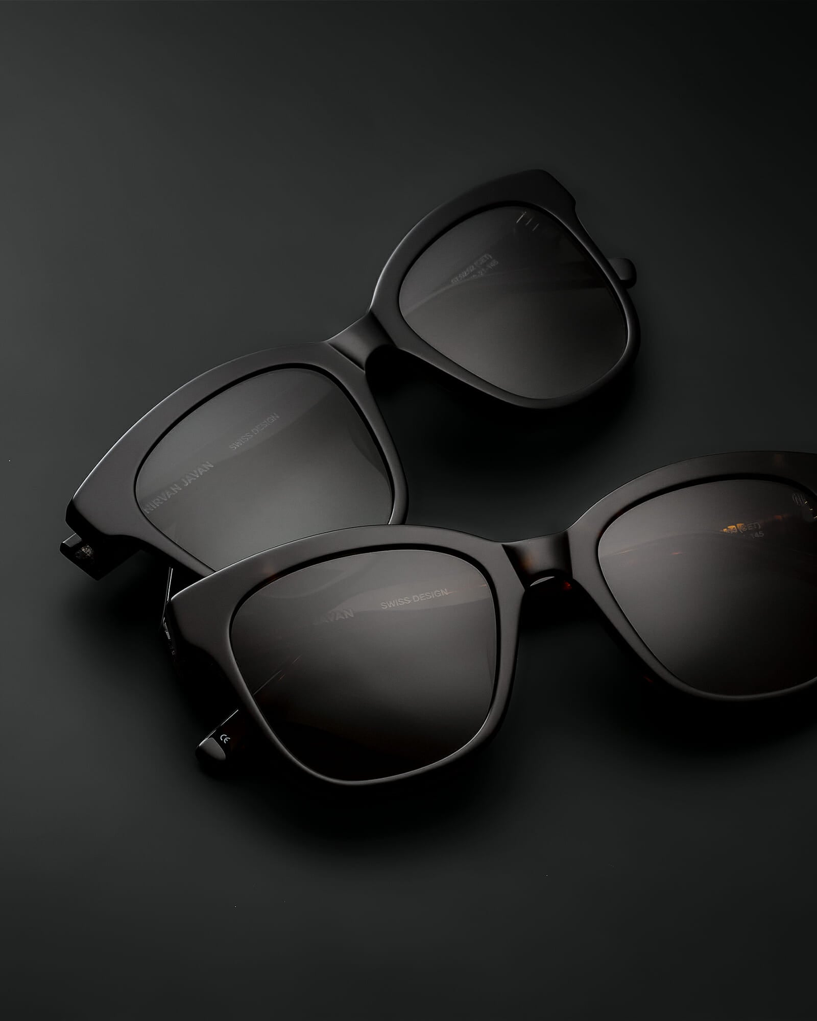 Two cat eye acetat shades, one in black with grey lenses, one in brown with brown lenses on a black background, the frames are folded