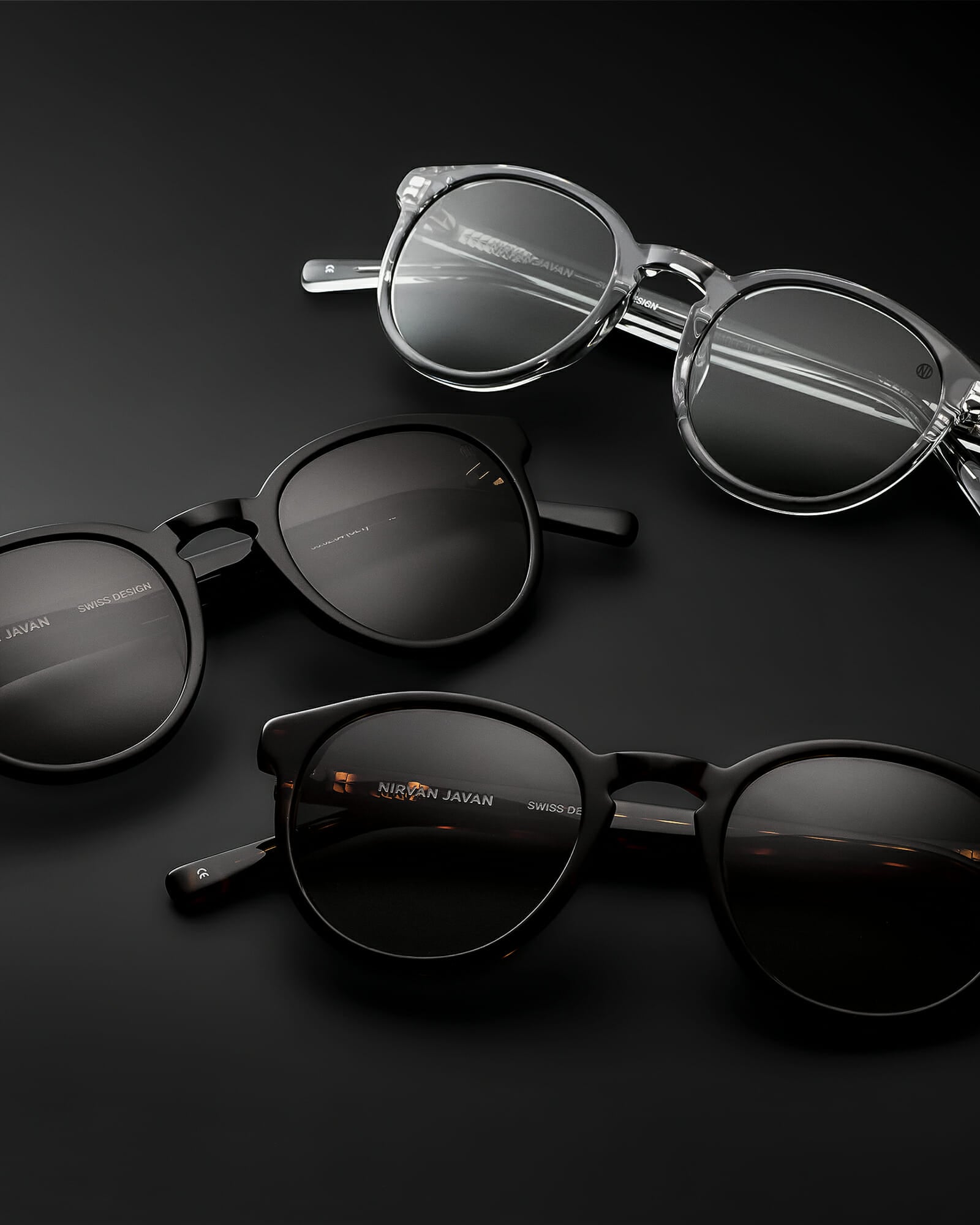 Three round acetat shades, one in black with brown lenses, one in brown with grey lenses and one in transparent with grey lenses on a black background, the frames are folded